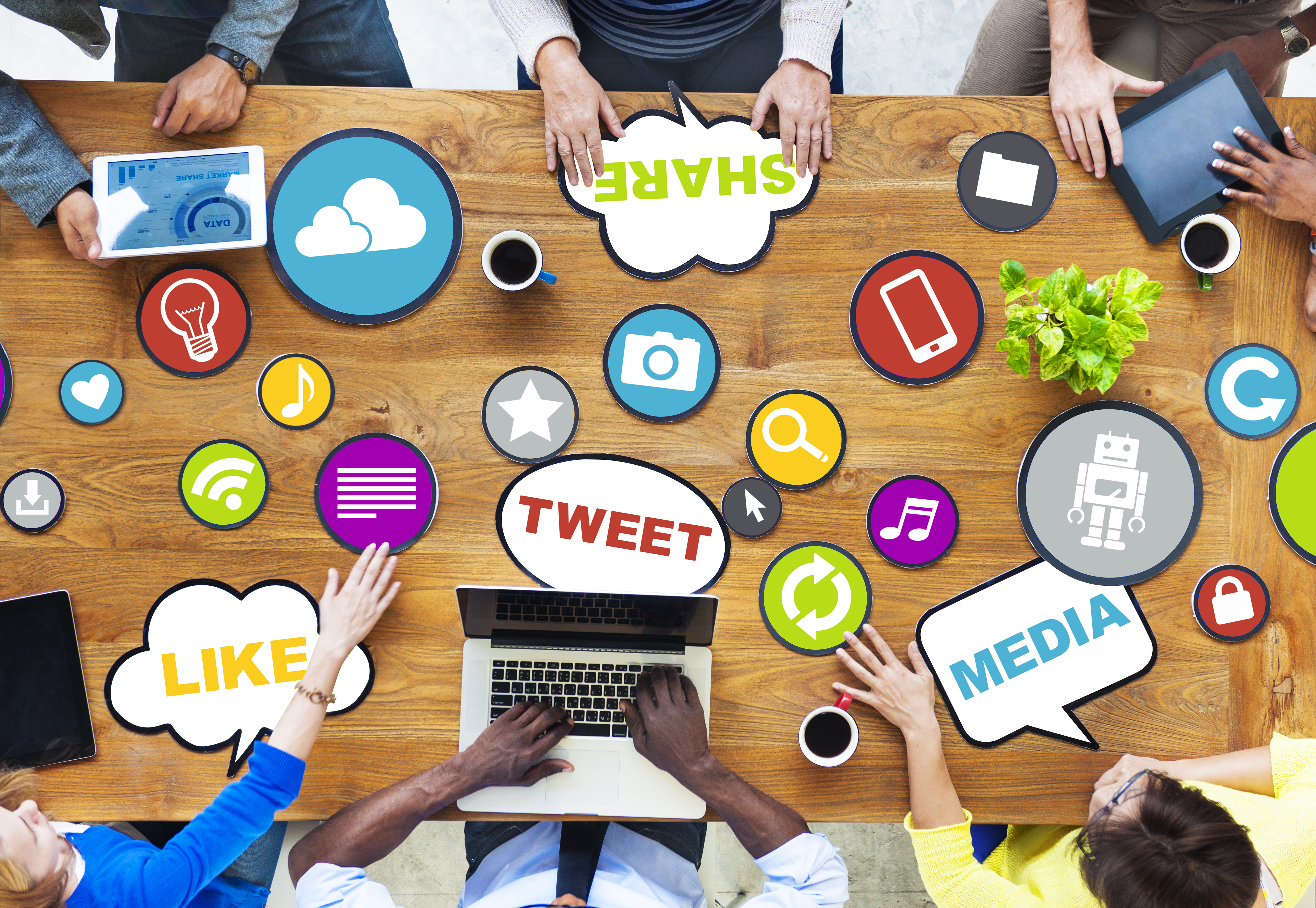 A top down image shows a desk with multiple people around it; speech and thought bubbles, along with icons, give them impression they are discussing social media.